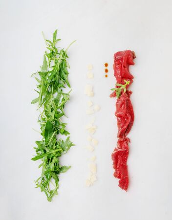 Concept of a  tricolour Italian flag. Fresh arugula salat as a green pale. Slices of parmesan chees as a white pale. Marbled beef carpaccio as a red pale.の写真素材