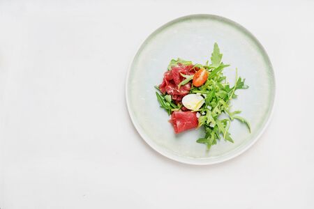 Marbled beef carpaccio on the plate with  fresh arugula salat, slices of parmesan cheese and sliced hard-boiled egg and tomato. Top view.の写真素材