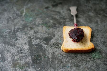 Spoon of raspberry jelly on the slice of toasted bread over rustic metal background. Selective...