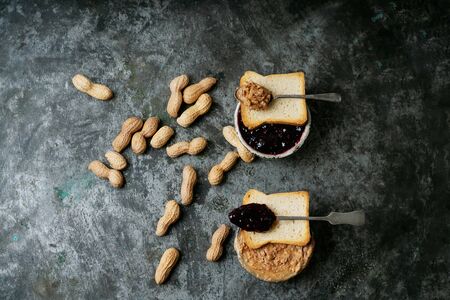 Peanut butter and raspberry jelly bowls with crispy toasts over rustic metal background with peanuts...
