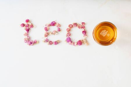 Cup of herbal tea over white marble background. Food typography. Word "tea" made of dry globe amaranth flowers. Top view. Copy space.の写真素材