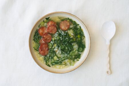 Caldo Verde Soup with greens and chopped chorizo on the top in ceramic bowl with ceramic spoon. Top Viewの写真素材