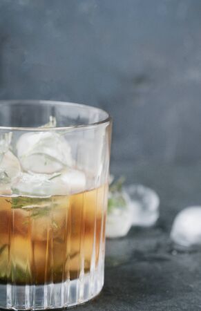 Misted glass of whiskey on the rocks served with frozen herbs in ice cubes over the dark background. Side view. Selective focus.の写真素材