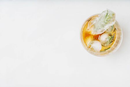 Single glass of whiskey on the rocks served with frozen herbs in ice cubes over the white background. Top view. Copy spaceの写真素材