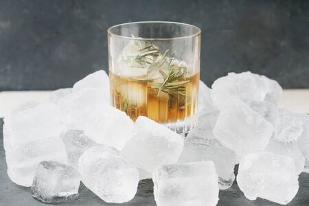 Misted glass of whiskey on the rocks served with frozen herbs in ice cubes over the ice heap. Side view. Selective focus.の写真素材