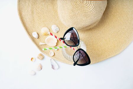 Summertime concept. Beach set: sunglasses, shells and glass with straws over summer hat on the white background. Top view.の写真素材