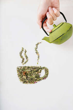 Dry herbal tea leaves spilled from the strainer and scattered in shape of cup with smoke  over white background. Creative concept. Top viewの写真素材