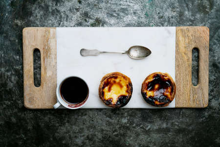 Pastel de Nata. Traditional Portuguese dessert, egg tart on the wooden marble board with cup of coffee over metal rustic background. Top viewの写真素材