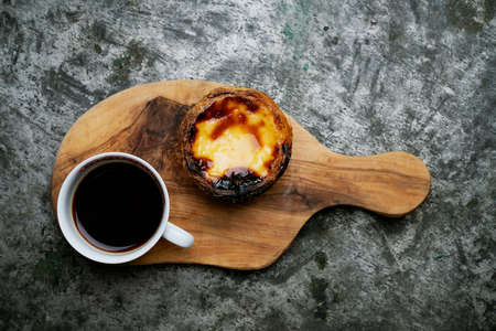 Pastel de Nata. Traditional Portuguese dessert, egg tart on the board with cup of coffee over metal...
