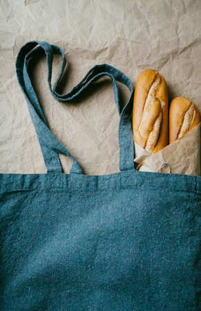 Traditional French baguette wrapped in brown paper over wooden background. Sustainable package zero waste concept. Flat lay. Top Viewの写真素材