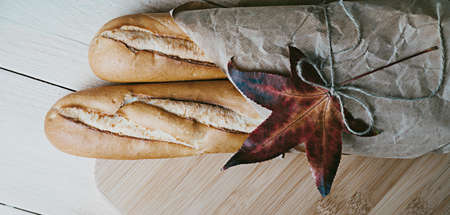 Traditional French baguette wrapped in brown paper over wooden background. Sustainable package zero...