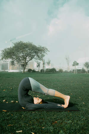 Young woman doing yoga, stretching, exersice, workout  in the park using yoga mat. Natural beginner yoga posing. Healthcare concept.の写真素材