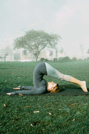 Young woman doing yoga, stretching, exersice, workout  in the park using yoga mat. Natural beginner yoga posing. Healthcare concept.の写真素材