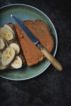 Home made vagan sandwich wth peanut butter and banana served on ceramic plate with vintage knife over rustic metal background. Vegan breakfast concept. Top View. Flat Layの写真素材