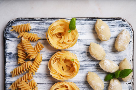 Traditional Italian pasta: Tagliatelle, fusilli and gnocchi  decorated with basil leaves over a white background.  Italian food concept. Top View. Flat Layの写真素材