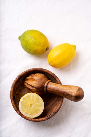 Lemons with wooden olive tree squeezer  and a bowl over a white textile background. Top View. Flat Lay.の写真素材