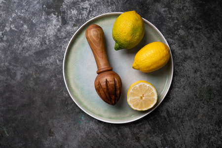 Lemons with wooden Juicer over a blue ceramic plate. Flat Lay. Top View. Copy Space