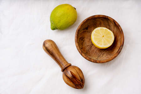 Lemon  in wooden olive tree bowl with wooden squeezer. cut in half.  white textile background. Top View. Flat Lay. Copy Spaceの写真素材