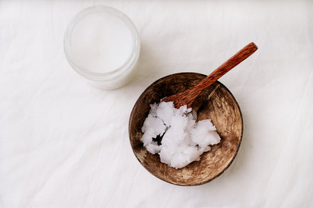 Organic coconut oil in the glass jar and in coconut bowl with coconut spoon over white textile background. Sustainability concept. Top View. Flat Lay.の写真素材
