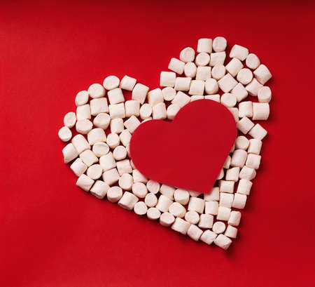 Heart symbol made from marshmallows with red card heart shaped in the center on red background. Top View. Flat Layの写真素材