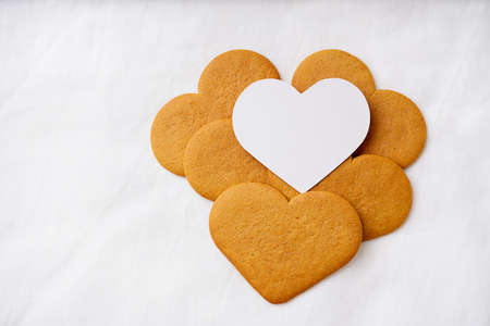 Heart shaped  gingerbread cookies with white card over a white textile background. Selective Focus. Copy space.の写真素材