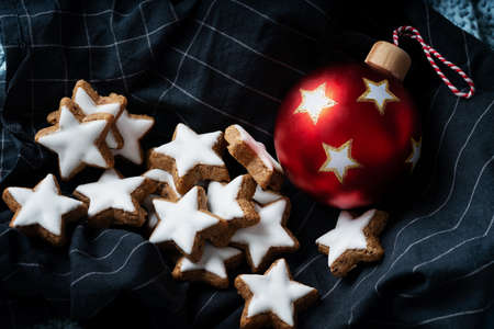 A selection of star glazed with white frosting over a dark blue napkin decorated with red Christmas ball. Close upの写真素材