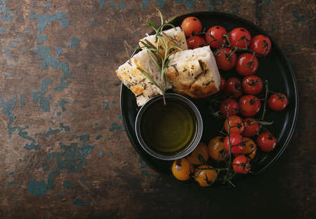 Traditional italian Appetizer home made foccacia bread served with olive oil and baked tomatoes and rosemary over a rustic wooden background. Top Viewの写真素材