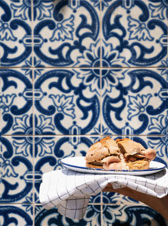 Man holding traditional portuguese Sandwich bifana over traditional portuguese background tiles...