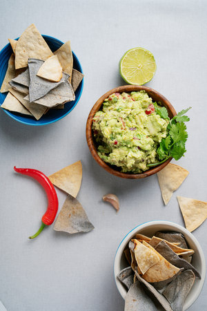A bowl of fresh guacamole garnished with cilantro, surrounded by blue and white tortilla chips, a...