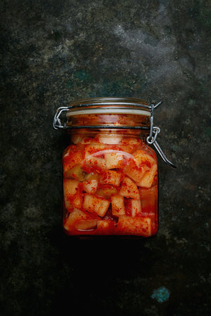 Glass jar filled with traditional Korean radish kimchi Kkakdugi, a spicy and fermented radish dish,...