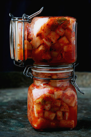 Glass jar filled with traditional Korean radish kimchi Kkakdugi, a spicy and fermented radish dish,...
