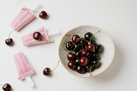 Bright cherry popsicles with fresh cherries on a white background, styled in a rustic bowl. Clean,...