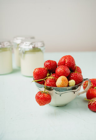 Fresh strawberries in a vintage cup, highlighted with yogurt jars in the background. The image emphasizes freshness and simplicity on a light background, ideal for summer vibes and healthy snacks.の写真素材