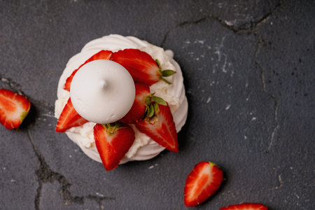 Top view of a meringue dessert with whipped cream and fresh strawberry slices on a dark textured background. Crisp details and vibrant colors enhance the composition.の写真素材