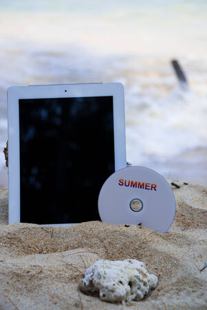 tablet and compact disk on sand in summer conceptの写真素材