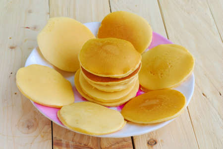 Stack of pancakes and syrup in plate on wooden table with green summer background