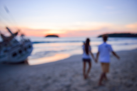 Blurred silhouette of couple walking hand in hand on sunset background, two people in love walking on the beach blur effectの写真素材