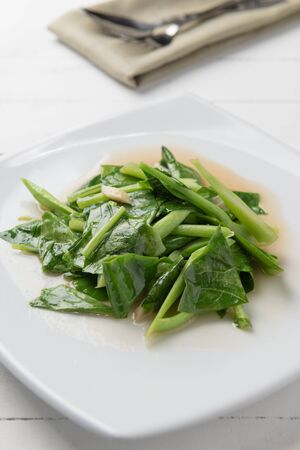 Kale stir fried in oyster sauce white plate on white tableの写真素材