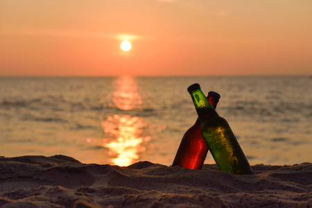 Ice cold brown and green Bottle of beer on the beach at sunsetの写真素材