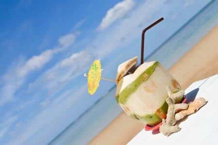 Coconut with drinking straw at the sea on white table