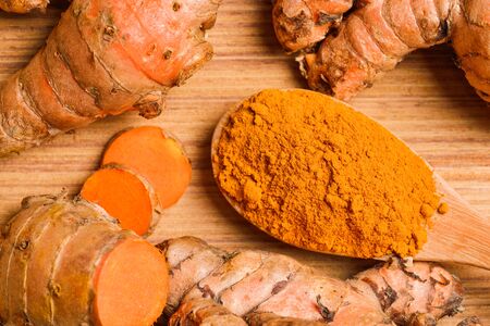 the turmeric powder in spoon and roots on wooden plateの写真素材
