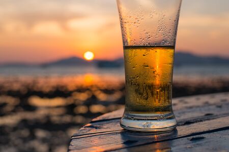 Glass of beer on a beach at sunsetの写真素材