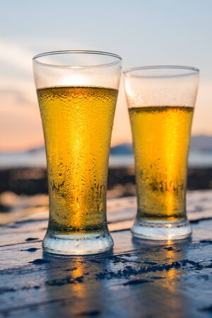 Glass of beer on a beach at sunsetの写真素材