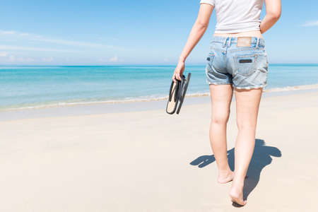 Young woman with sandals walking on beach in the sea in sunny hot dayの写真素材