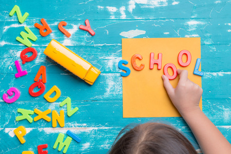 Children play plastic letters to combinations word "SCHOOL" on wood table.の写真素材