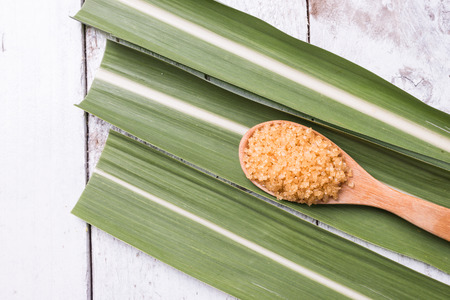 Spoonful of brown sugar on white rustic wooden background  and sugarcane leafの写真素材