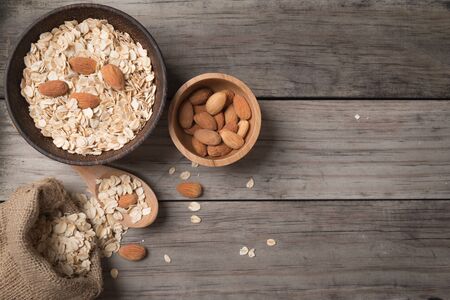 Dry rolled oat flakes oatmeal with almond nut on old wooden table retro filter