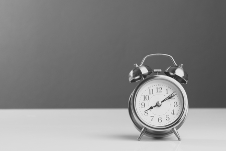 alarm clock showing eight o'clock on white table background, black and white image retro filter