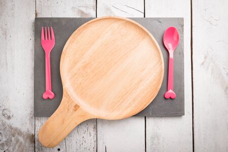 Empty Wooden plate pink plastic spoon and fork  on white rustic wooden backgroundの写真素材