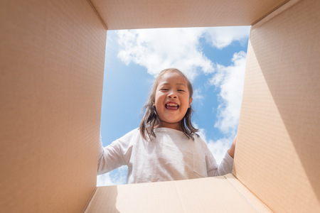 Asian kid girl age 6 year  unpacking and opening carton box, and looking inside with surpriseの写真素材